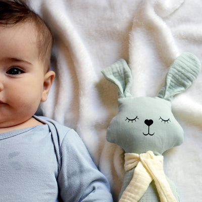 Baby lying on blanket beside aPunt Barcelona organic cotton rattle bunny