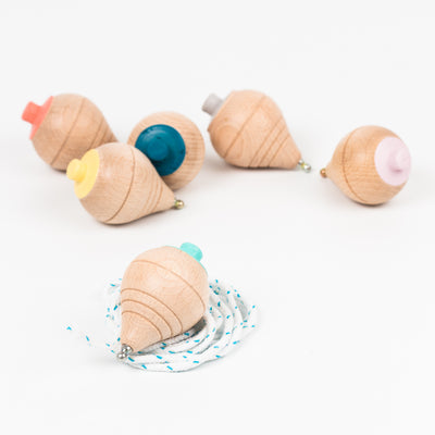 Yellow, coral, blue, grey, pink and mint wooden Me & Mine spinning tops lying on table
